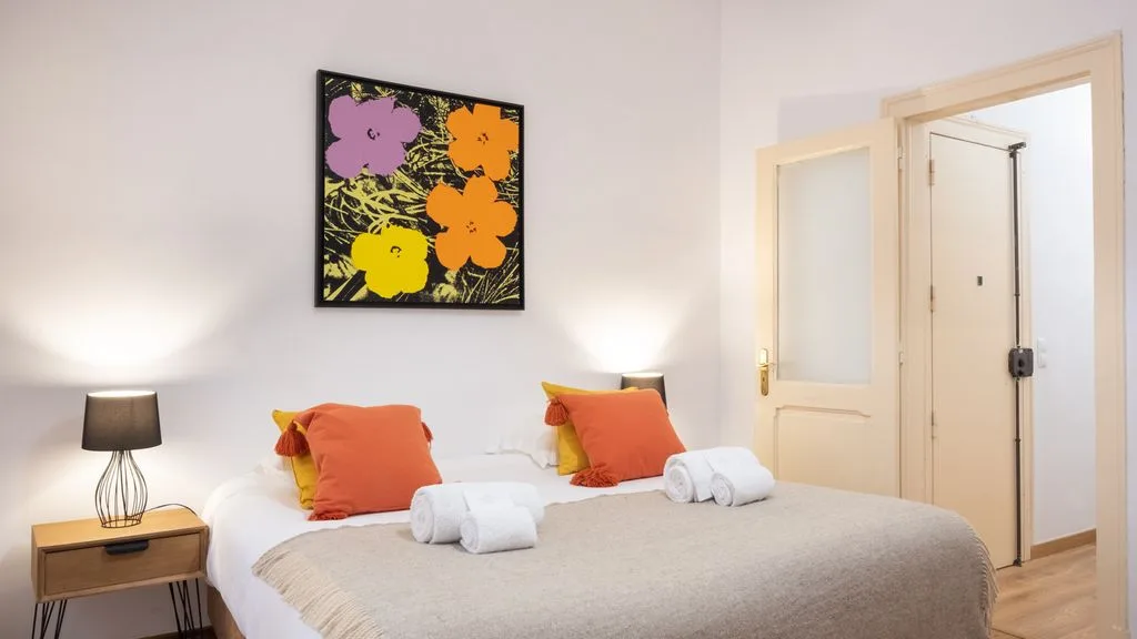 Un dormitorio con una cama, cojines coloridos y arte floral en la pared.