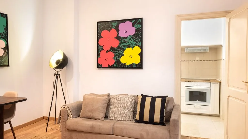 Una sala de estar con un sofá beige y un cuadro floral colorido.