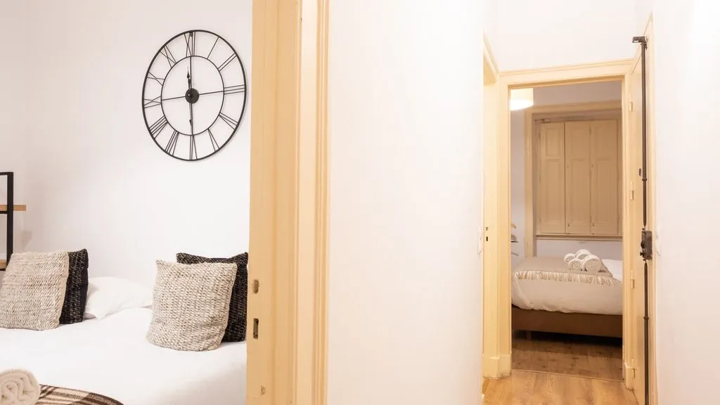 Un dormitorio con ropa de cama blanca y un reloj grande en la pared.