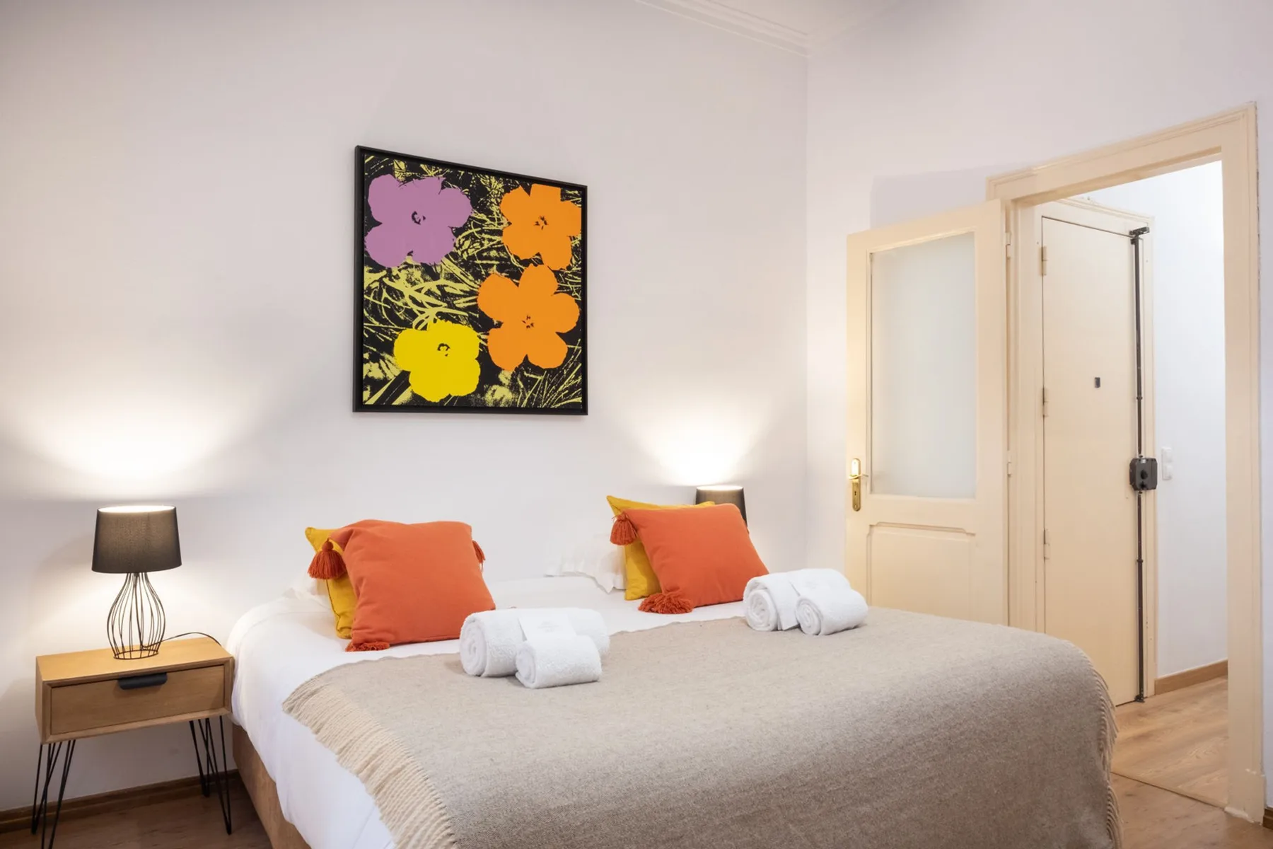 Un dormitorio con una cama bien arreglada, cojines coloridos y arte floral en la pared.