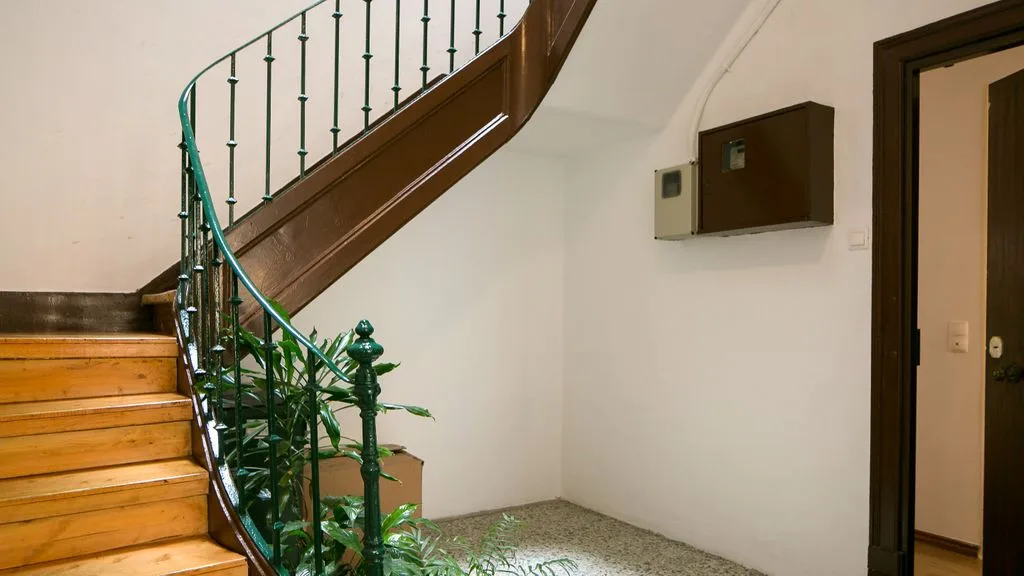 Una escalera interior con peldaños de madera, barandilla curva y una planta en maceta.
