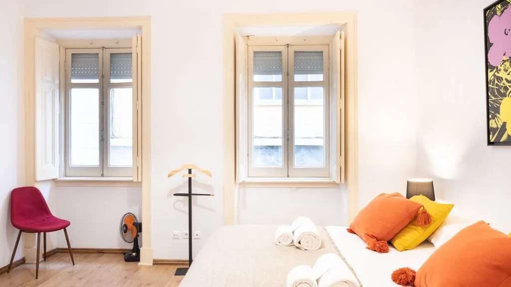 Un dormitorio luminoso con una cama y dos ventanas.