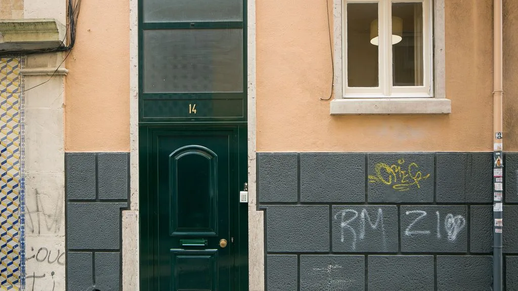 Entrada de un edificio a la calle con una puerta verde oscura y ventanas.