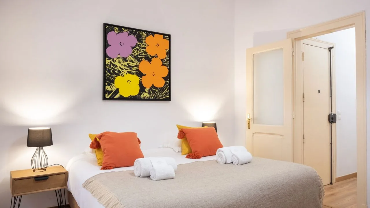 Un dormitorio con una cama bien tendida y un cuadro floral colorido encima.
