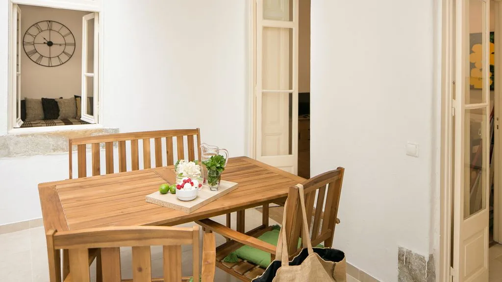 Una mesa de comedor de madera con sillas está junto a puertas abiertas en una habitación luminosa.