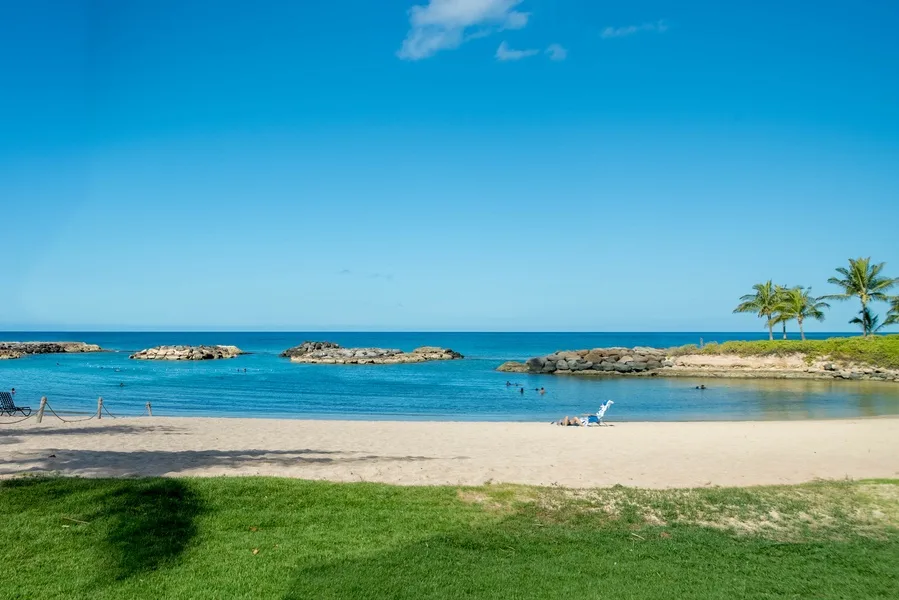 Una playa de arena bordea aguas tranquilas y azules, con césped en primer plano.
