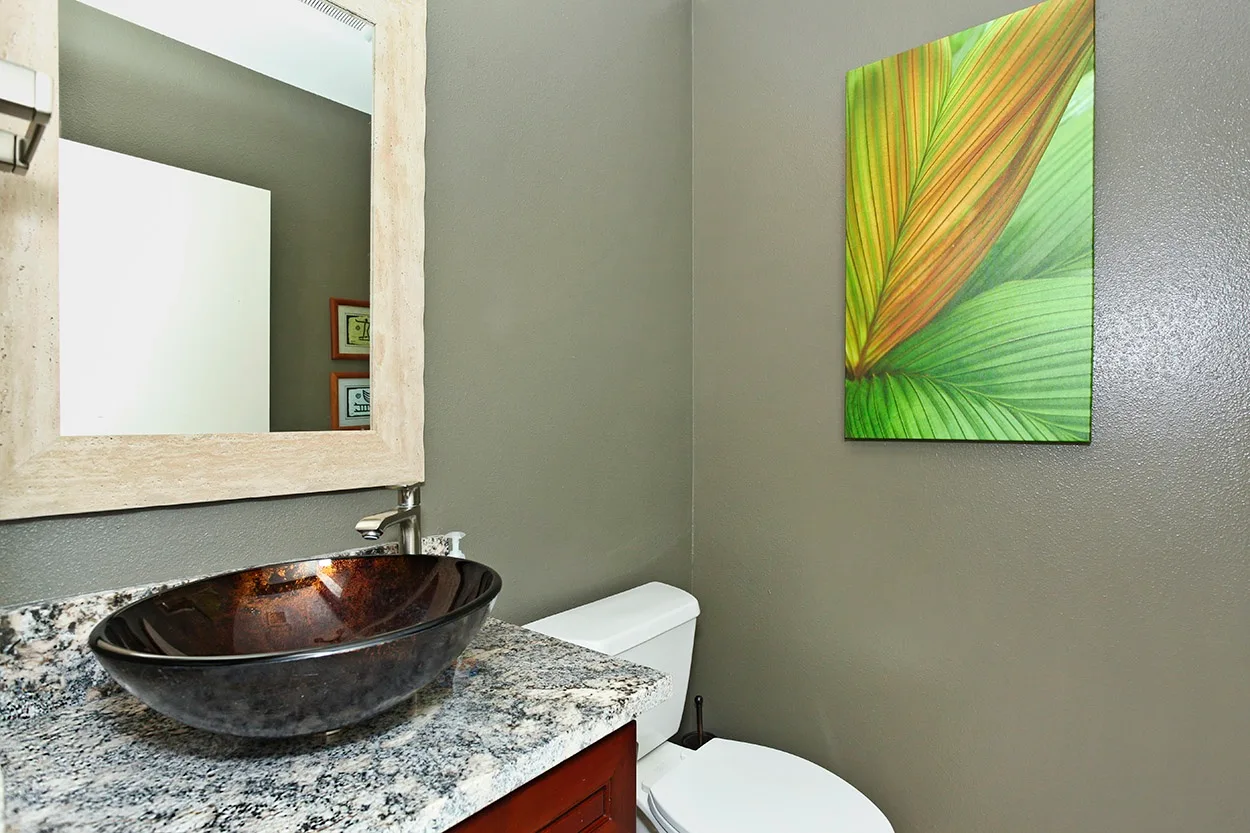 Un tocador de baño con lavabo oscuro sobrepuesto, espejo e inodoro.