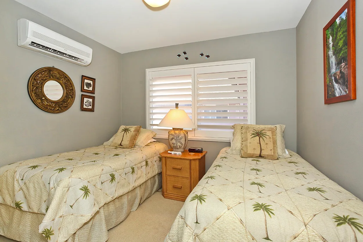 Un dormitorio con dos camas, ropa de cama con palmeras y una mesita de noche.
