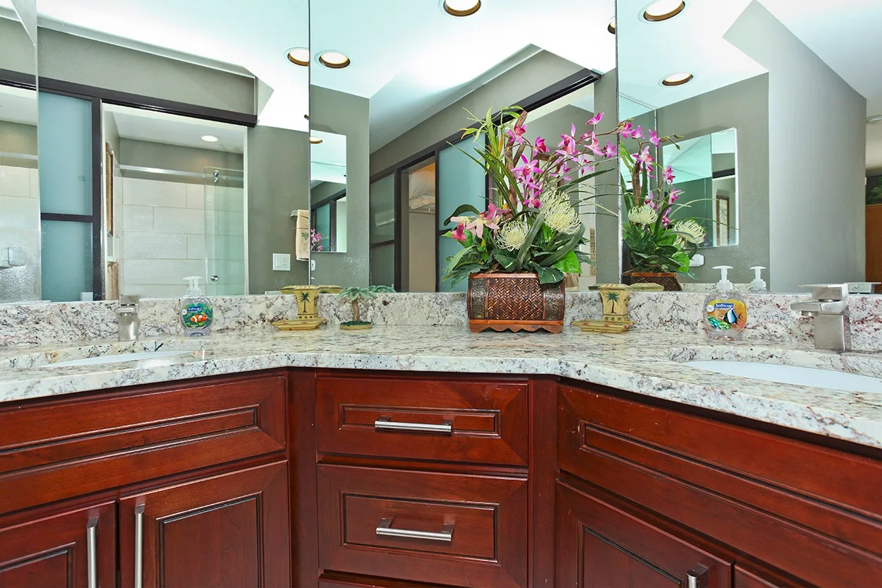 Un lavabo de baño con un espejo amplio y un arreglo floral sobre la encimera.
