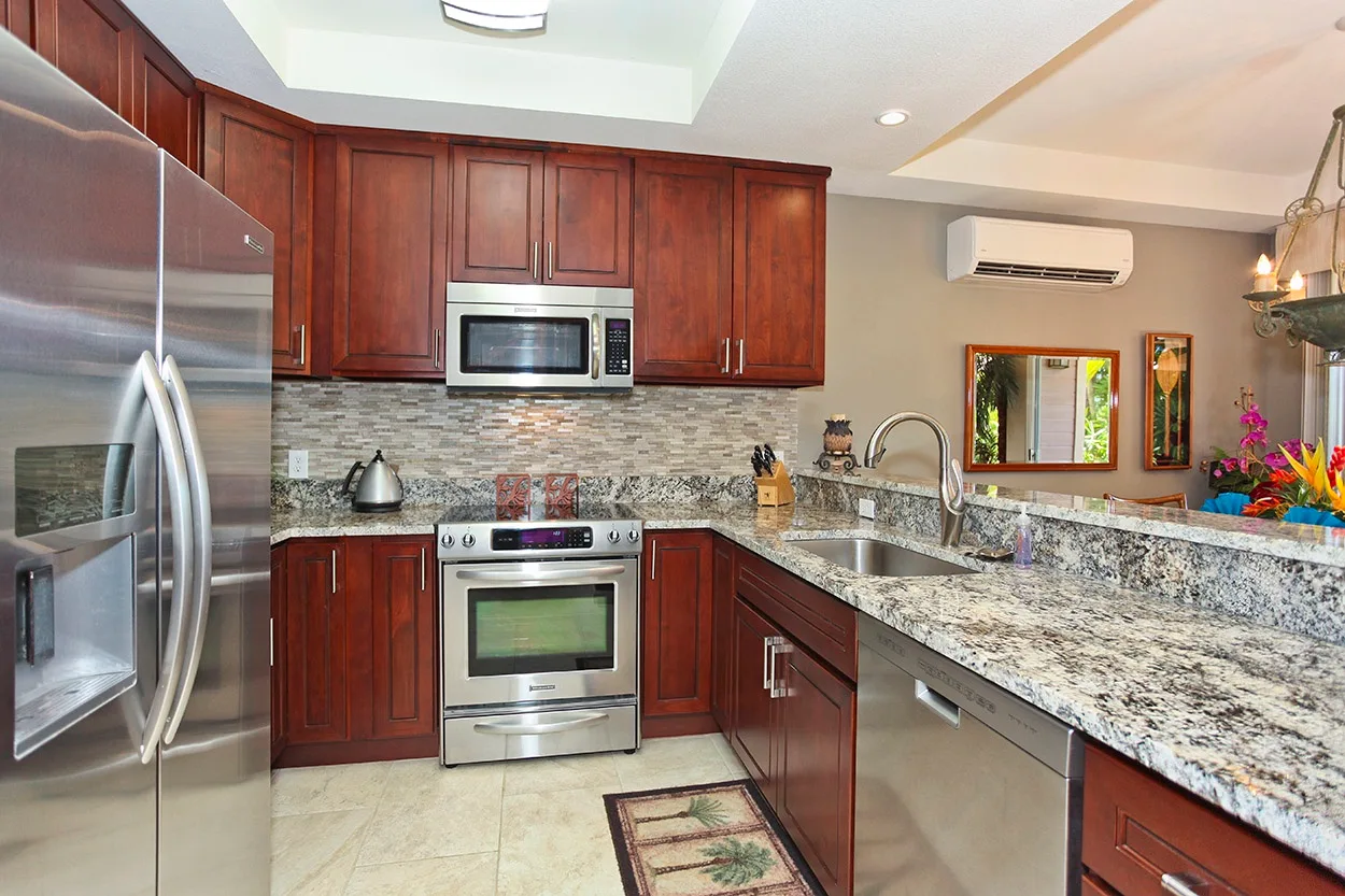 Una cocina con gabinetes de madera oscura, electrodomésticos de acero inoxidable y encimeras de piedra.