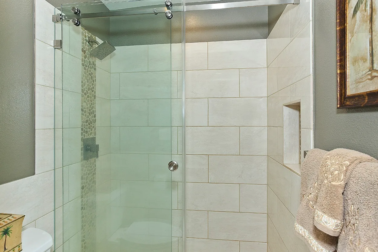 Una ducha de baño con azulejos, paneles de vidrio y una toalla colgada cerca.