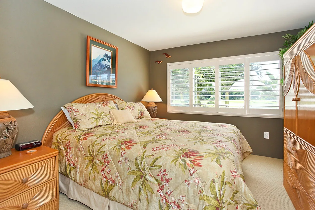 Un dormitorio con una colcha floral y una ventana amplia con contraventanas.