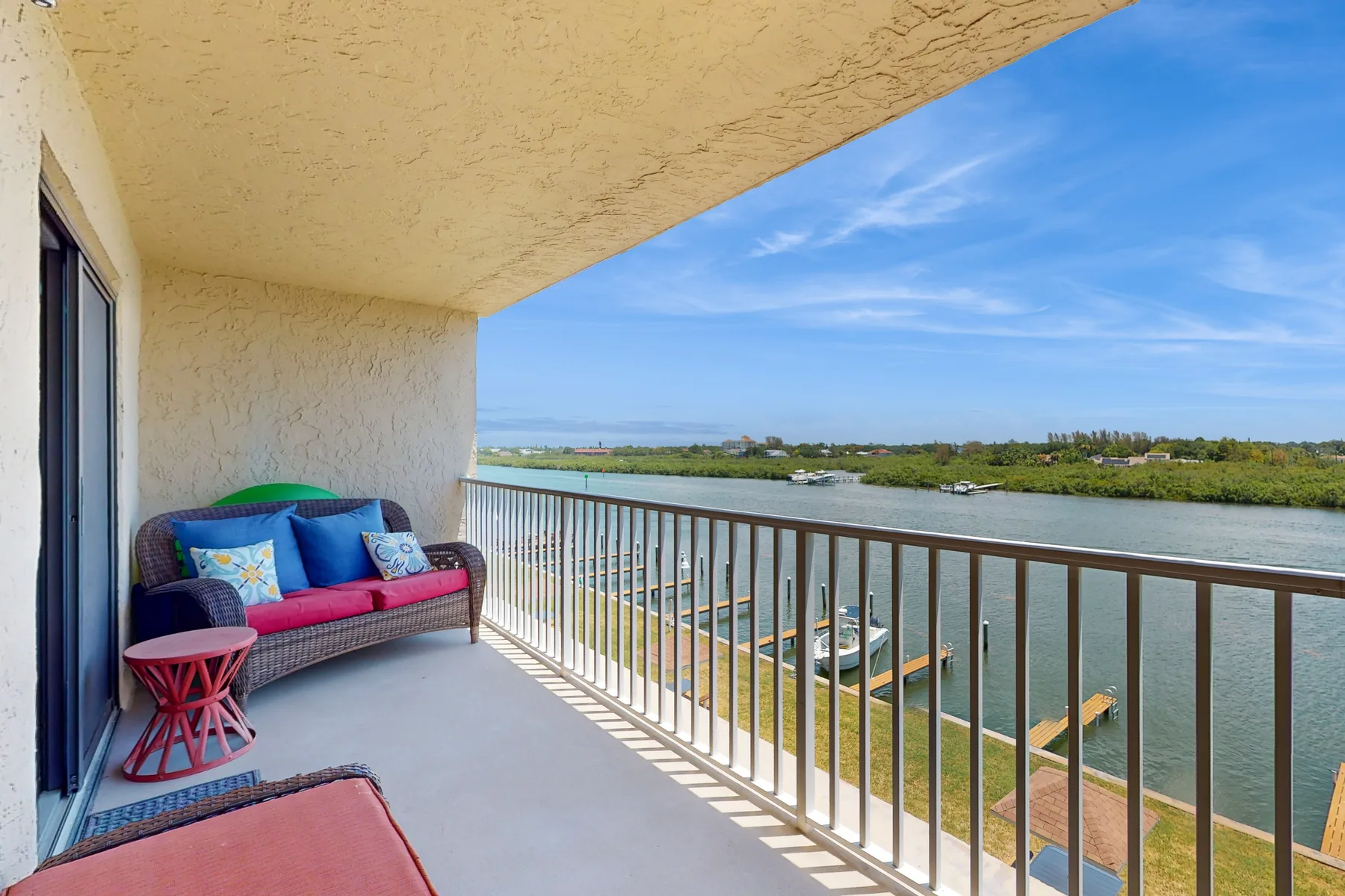 A covered balcony overlooks a river, with outdoor seating beside the railing.