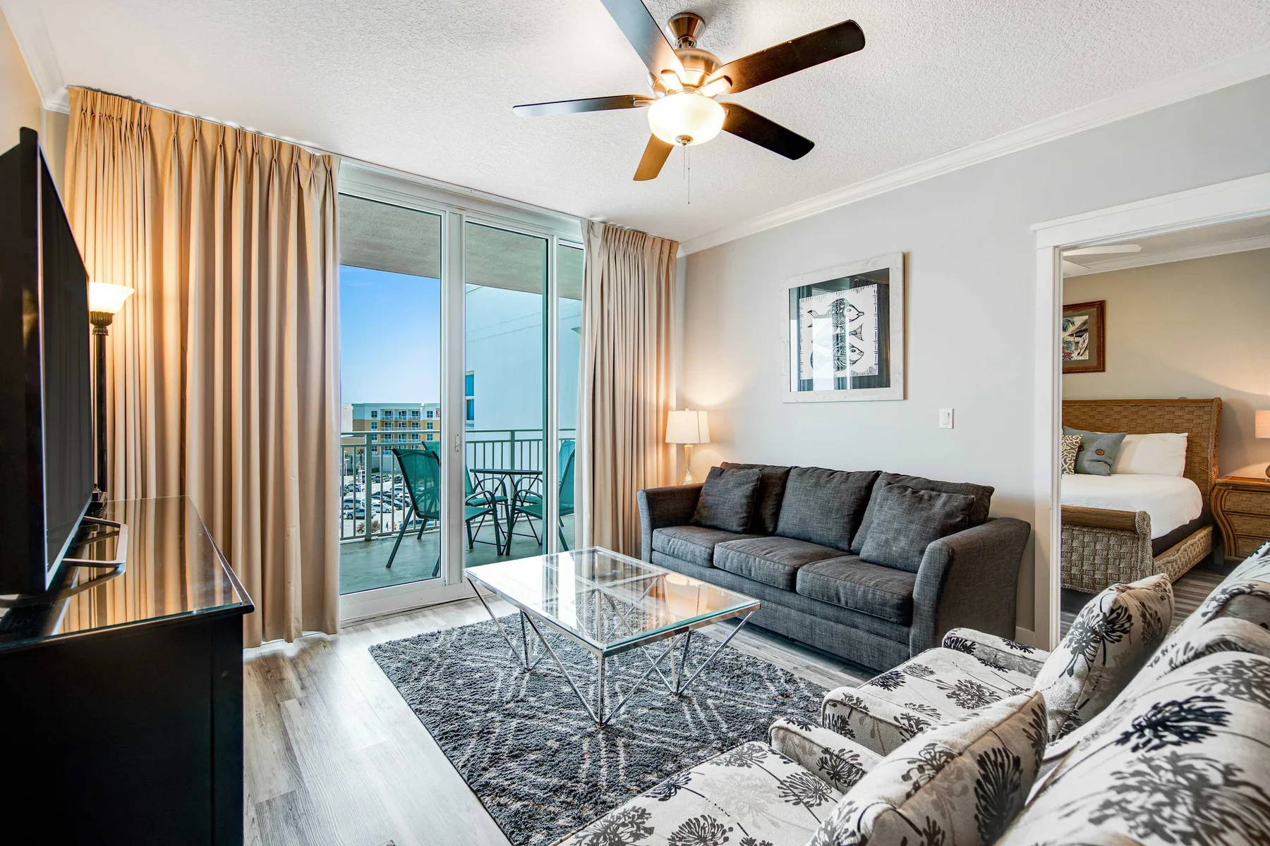 A living room with seating around a glass coffee table and sliding doors to a balcony.