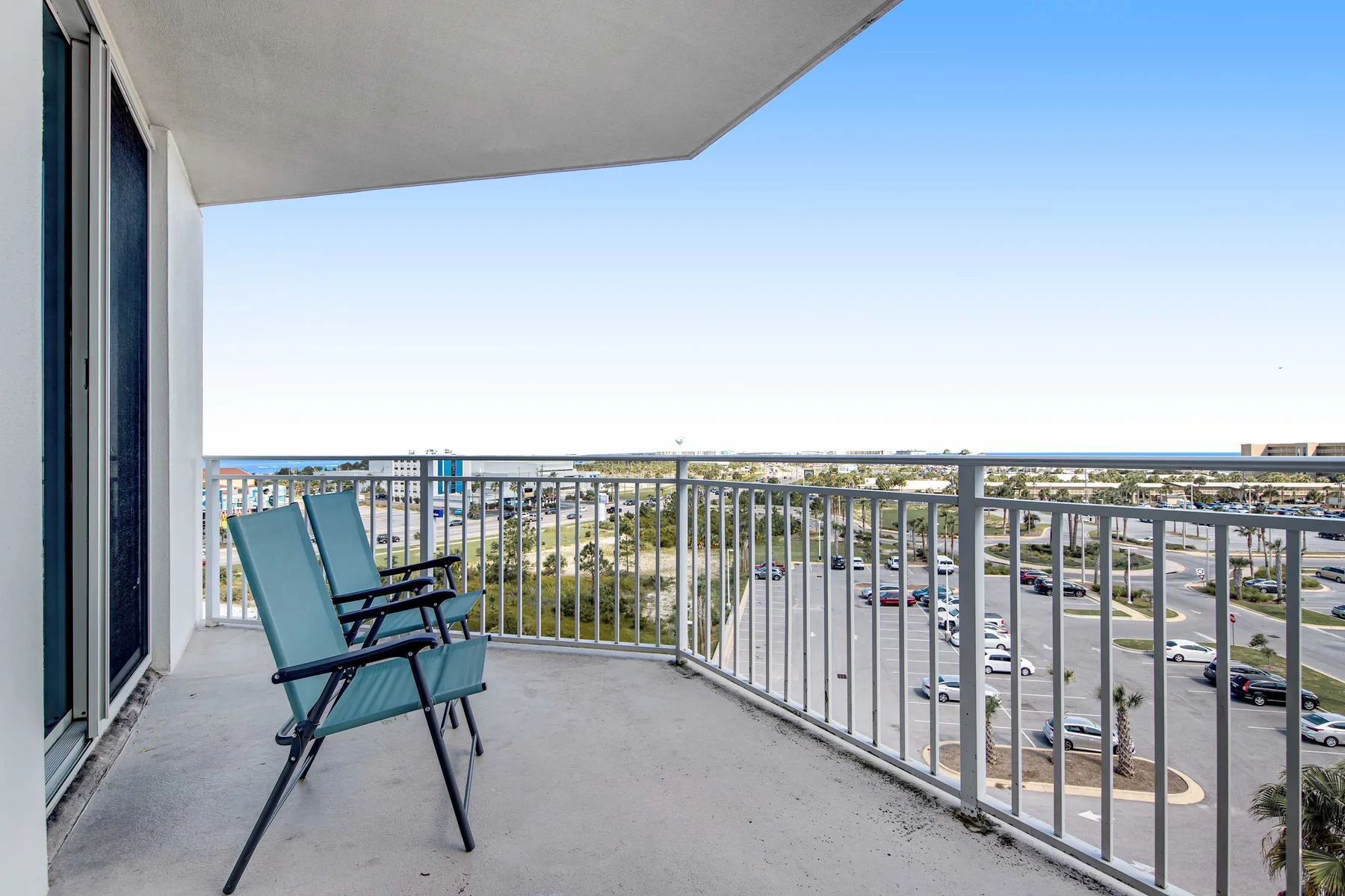 A balcony with seating overlooks a parking area and distant buildings.