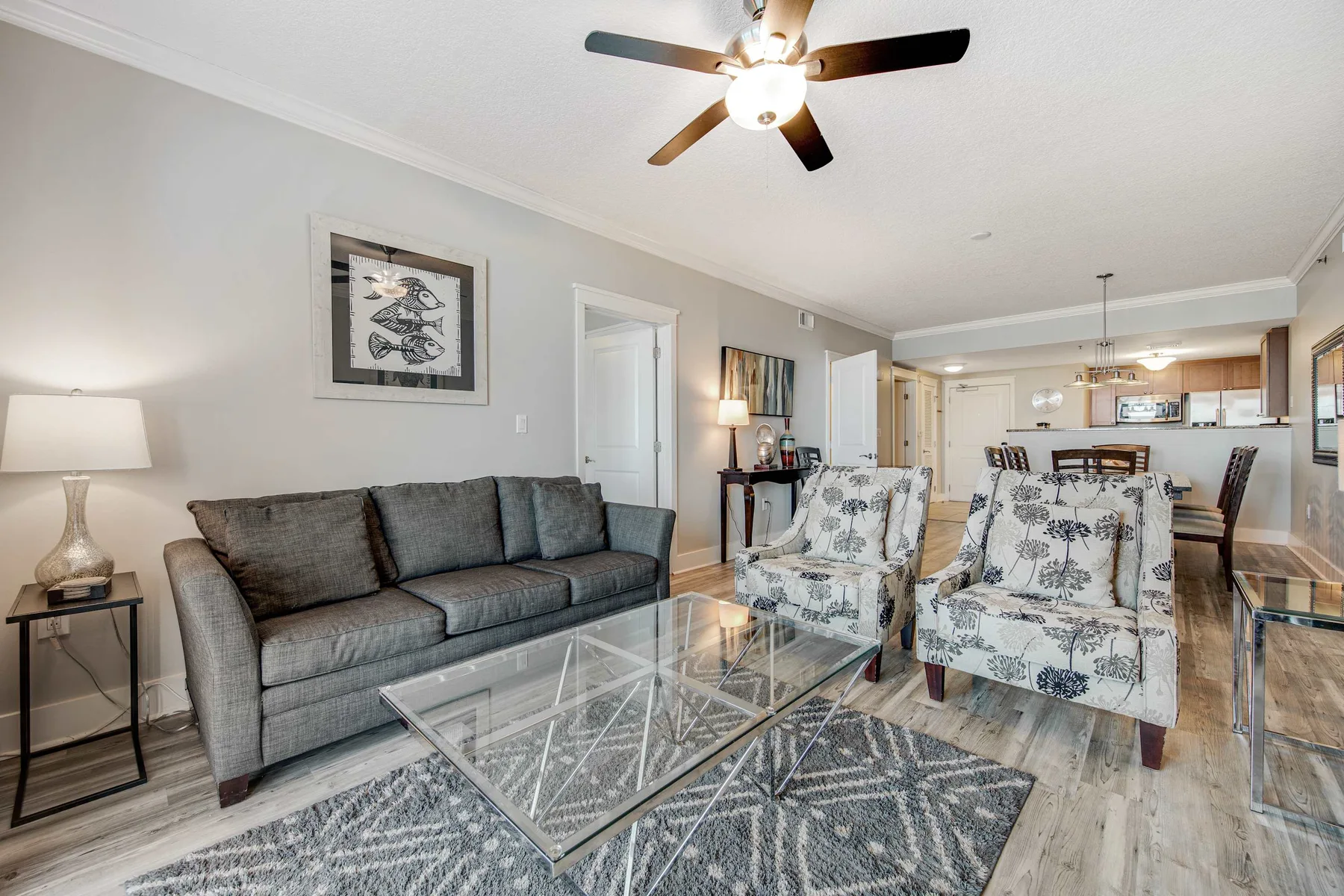 A living room with a gray sofa, patterned armchairs, and a glass coffee table.