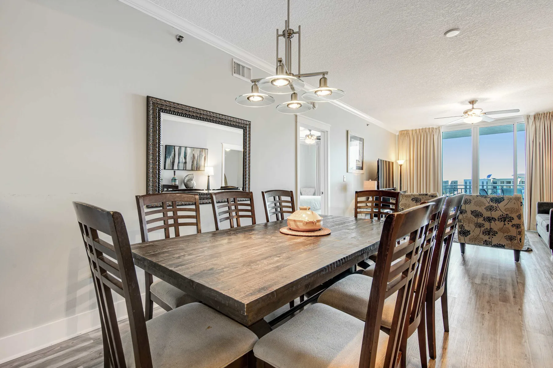 A dining area with a long wooden table and chairs beside large windows.