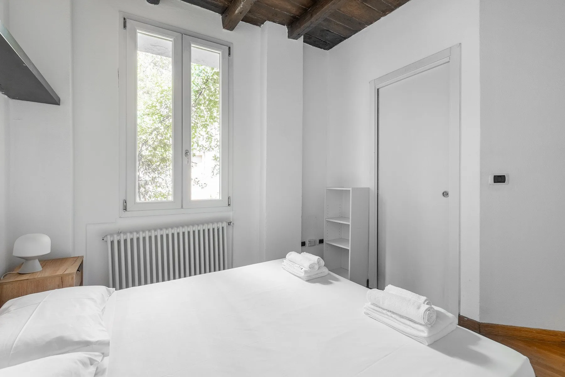 A bright bedroom with white bedding, a window, and a radiator.