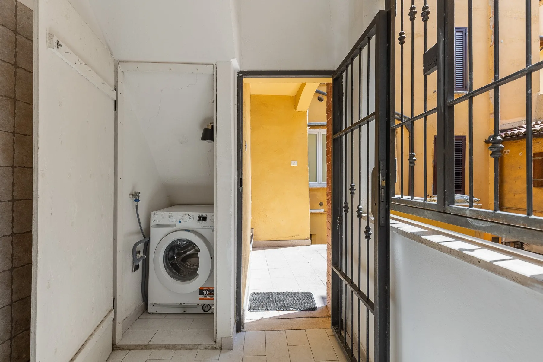 A laundry area opens onto a bright courtyard through a metal gate.