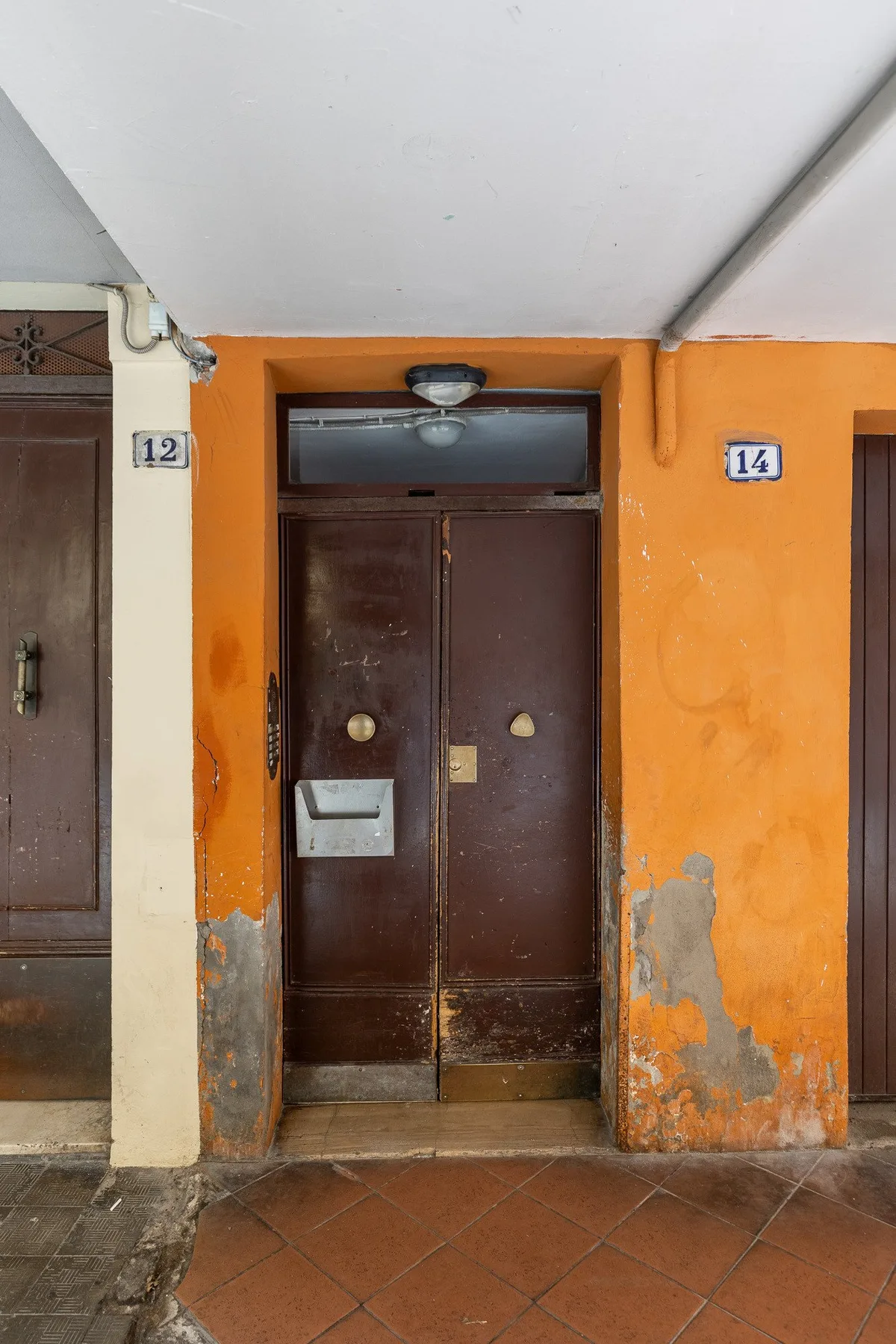 An apartment building entry with a dark double door set in an orange wall.