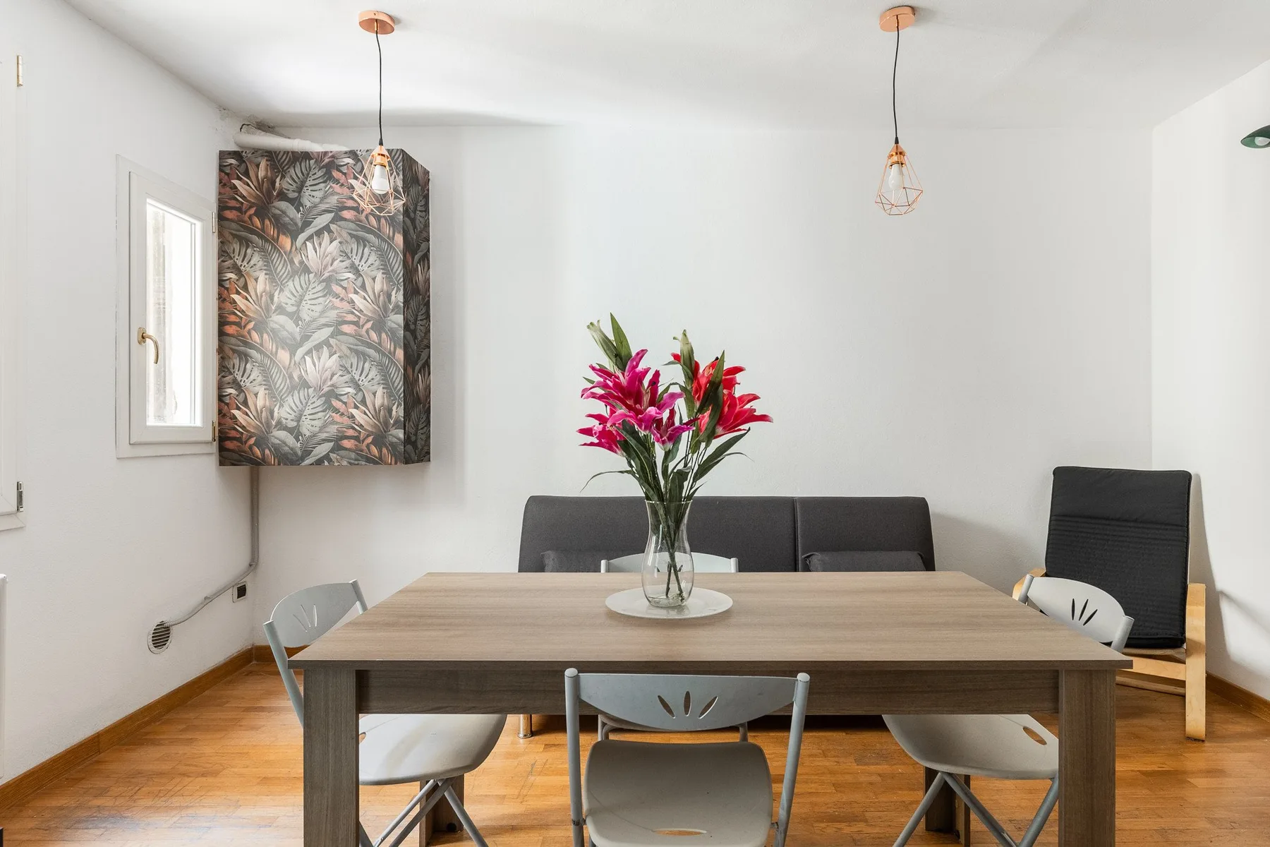 A dining area with a wooden table, chairs, and a vase of flowers.