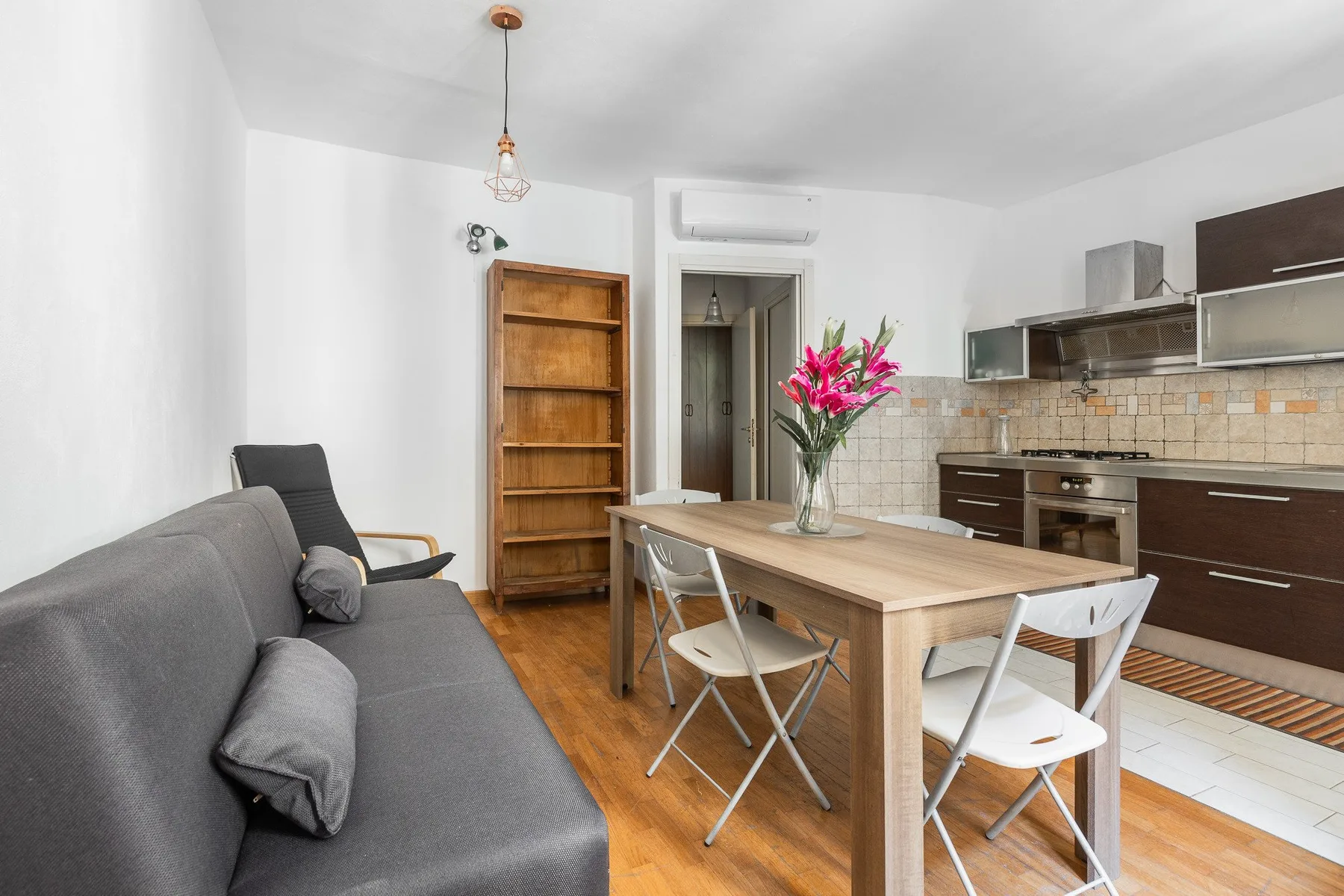 A bright kitchen and dining area with a table, seating, and a gray sofa.
