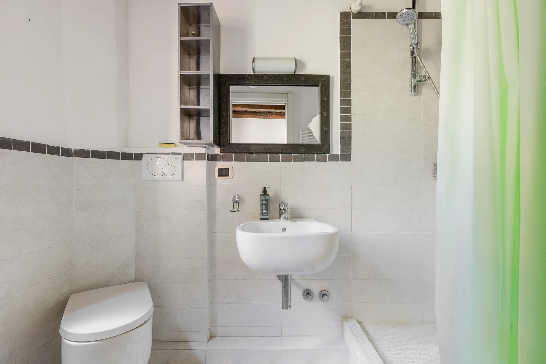 A tiled bathroom with a wall-mounted sink, toilet, mirror, and shower.