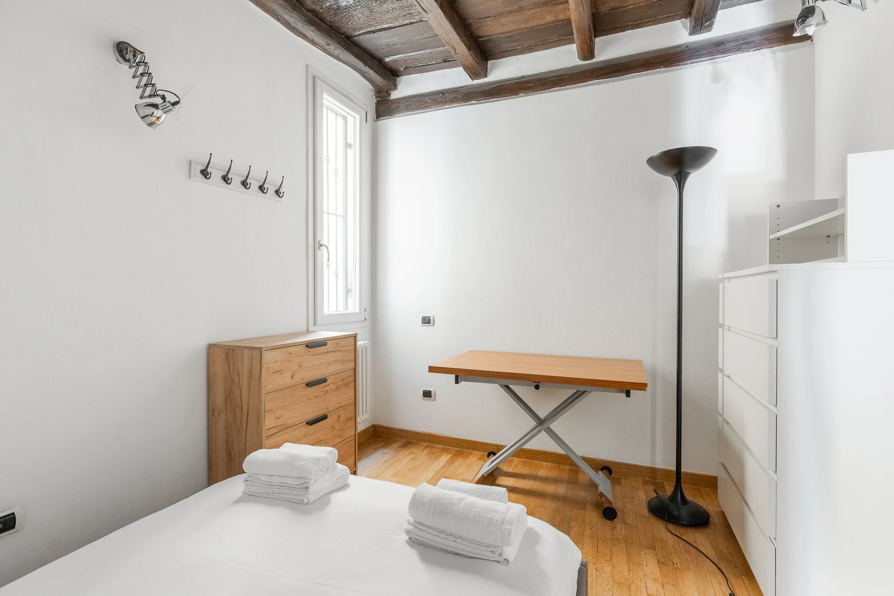 A bright bedroom with a bed, wooden dresser, and overhead beams.