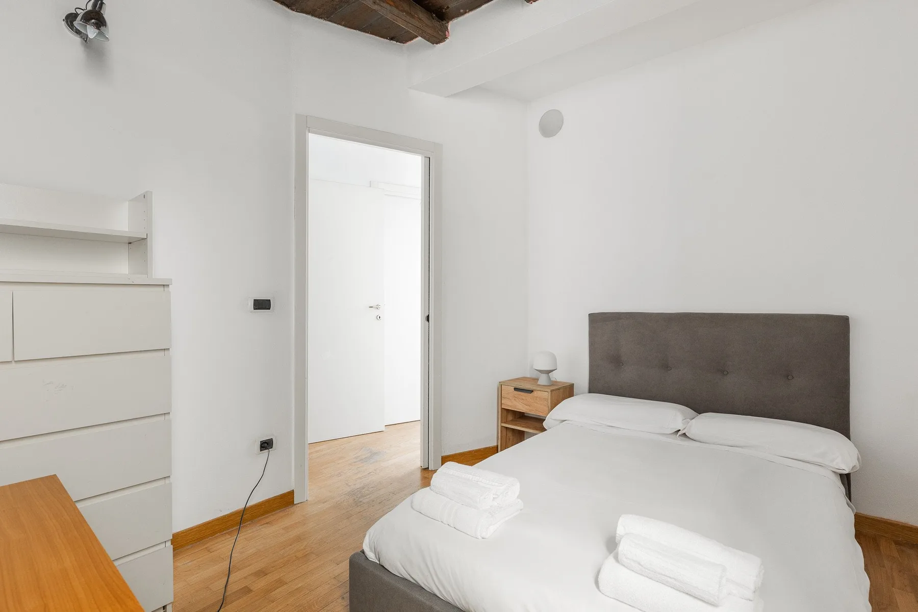 Un dormitorio luminoso con una cama tendida y paredes blancas.
