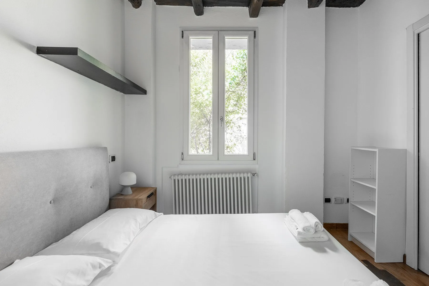 A bright bedroom with a bed beneath a window and a radiator.