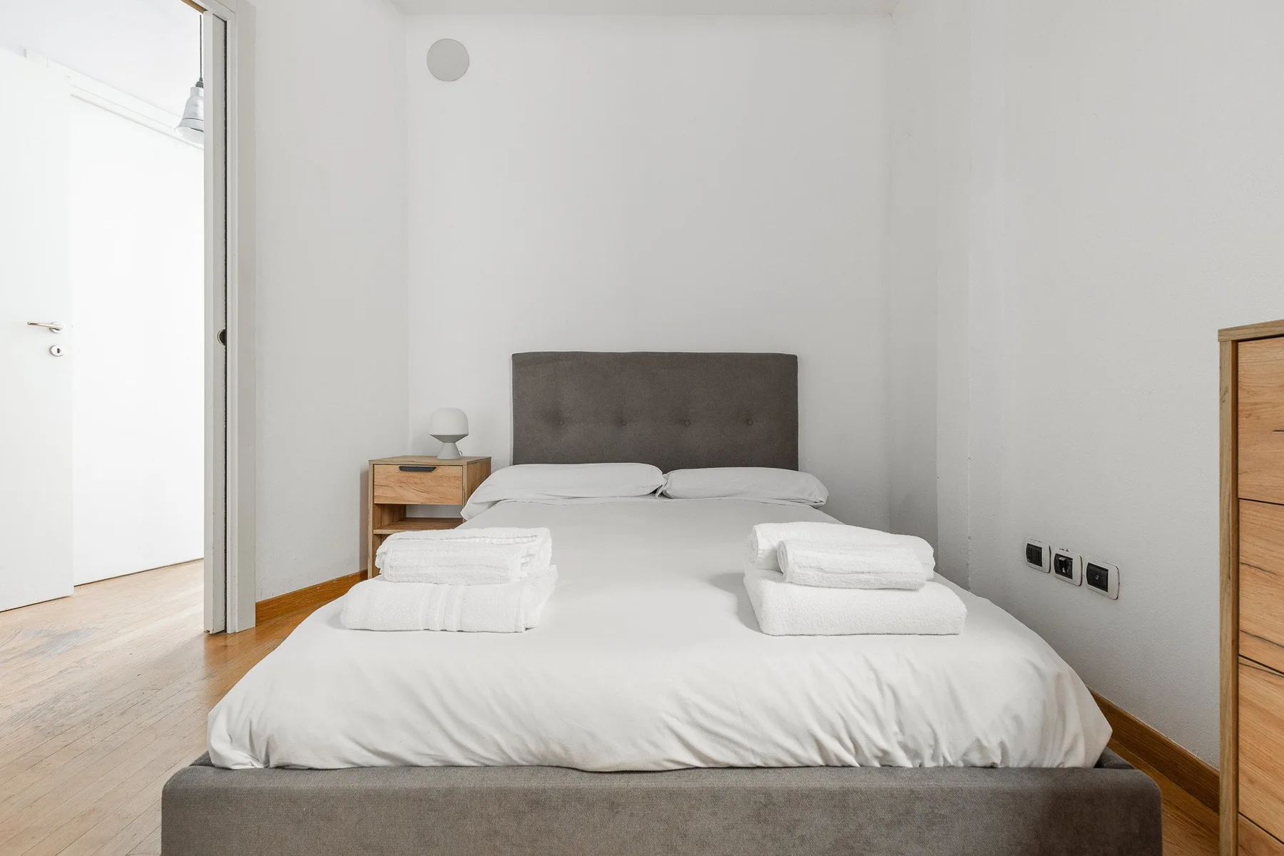 Bedroom with a neatly made bed, folded towels, and a small bedside table.