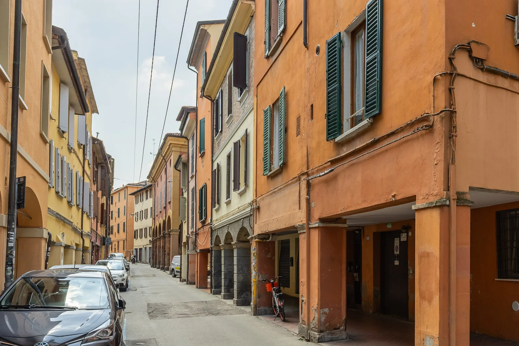 A narrow street lined with colorful buildings and parked cars.