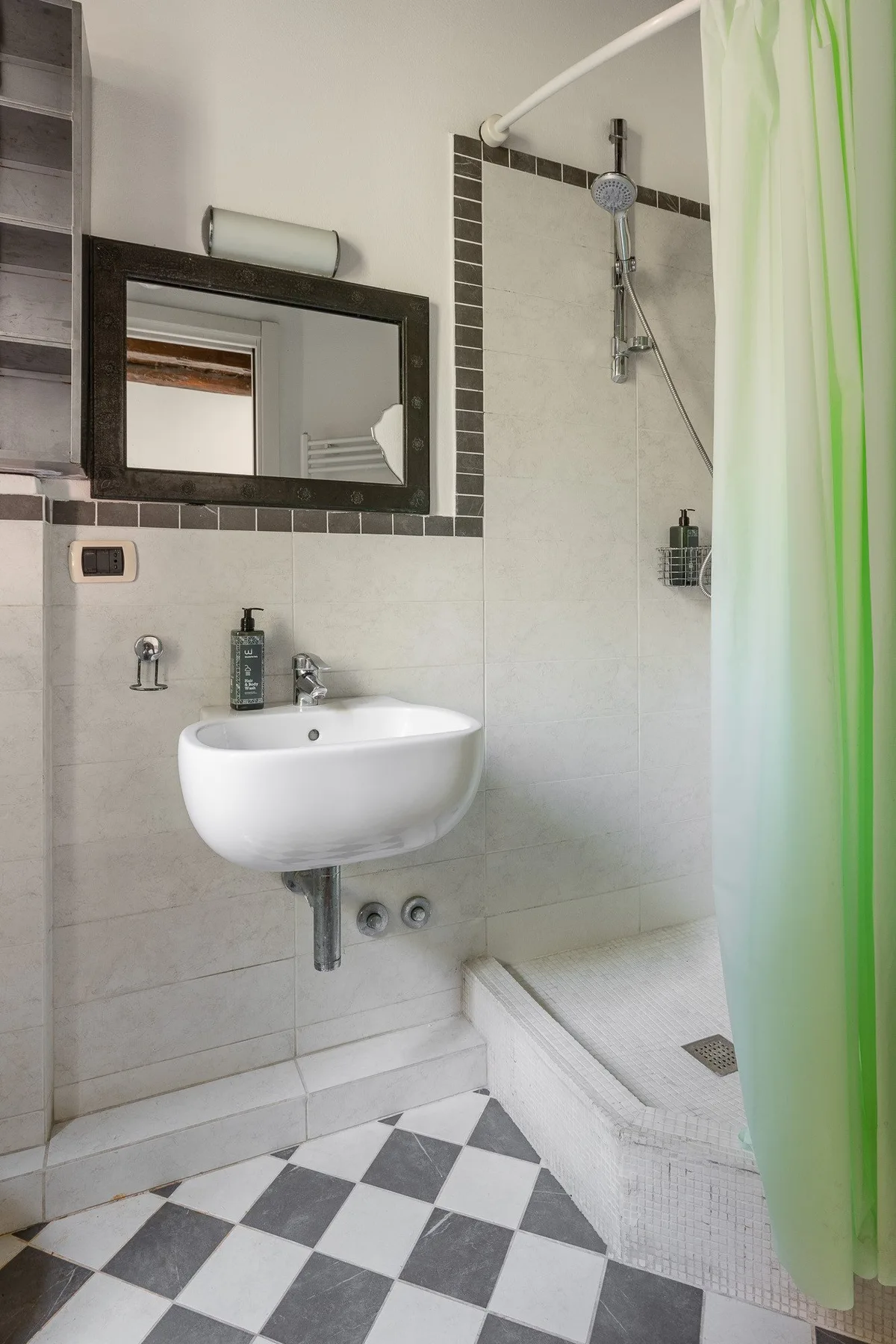 A bathroom with a wall-mounted sink and a shower behind a green curtain.
