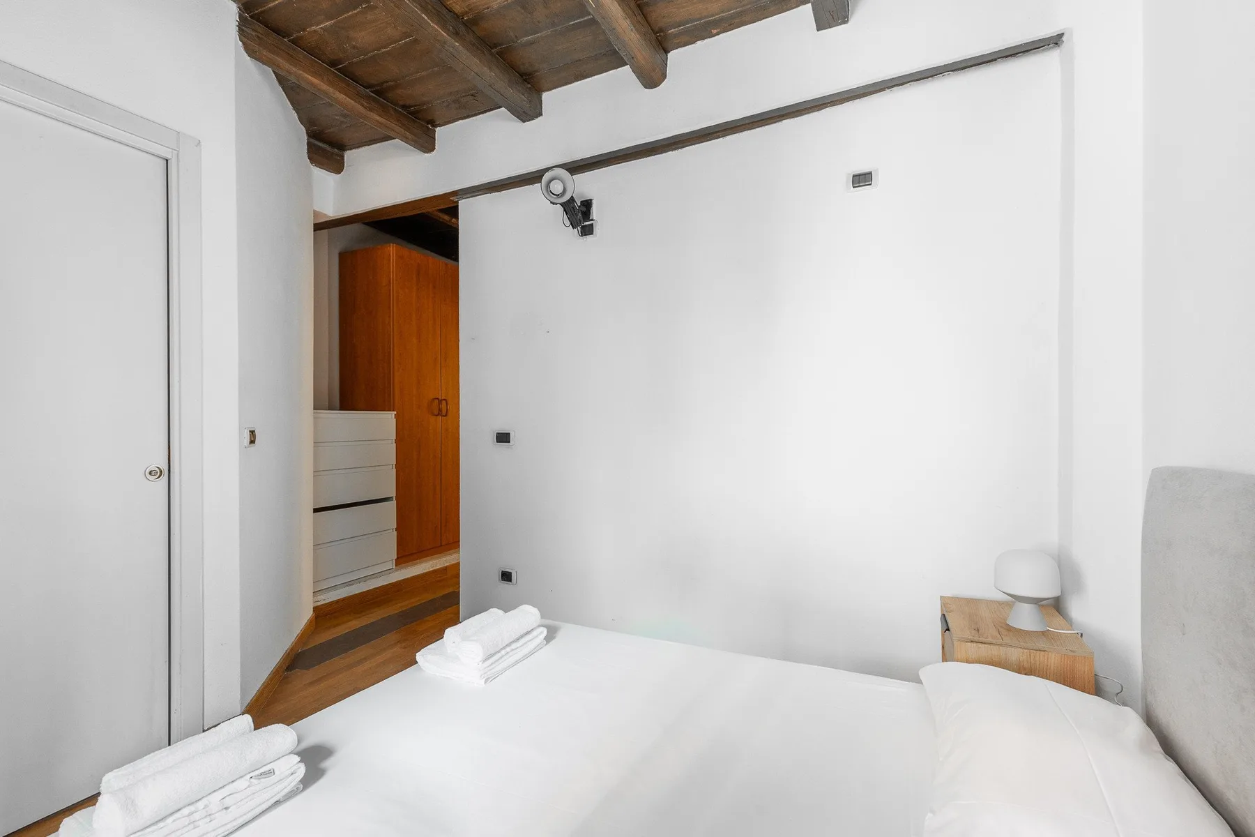 A bedroom with a bed beneath exposed wooden ceiling beams.