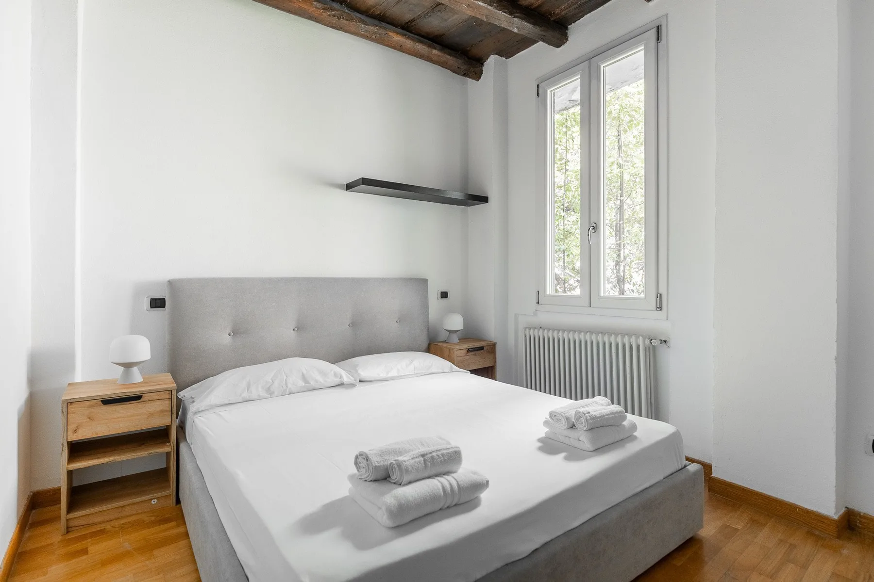 A bright bedroom with a neatly made bed and a window above the radiator.