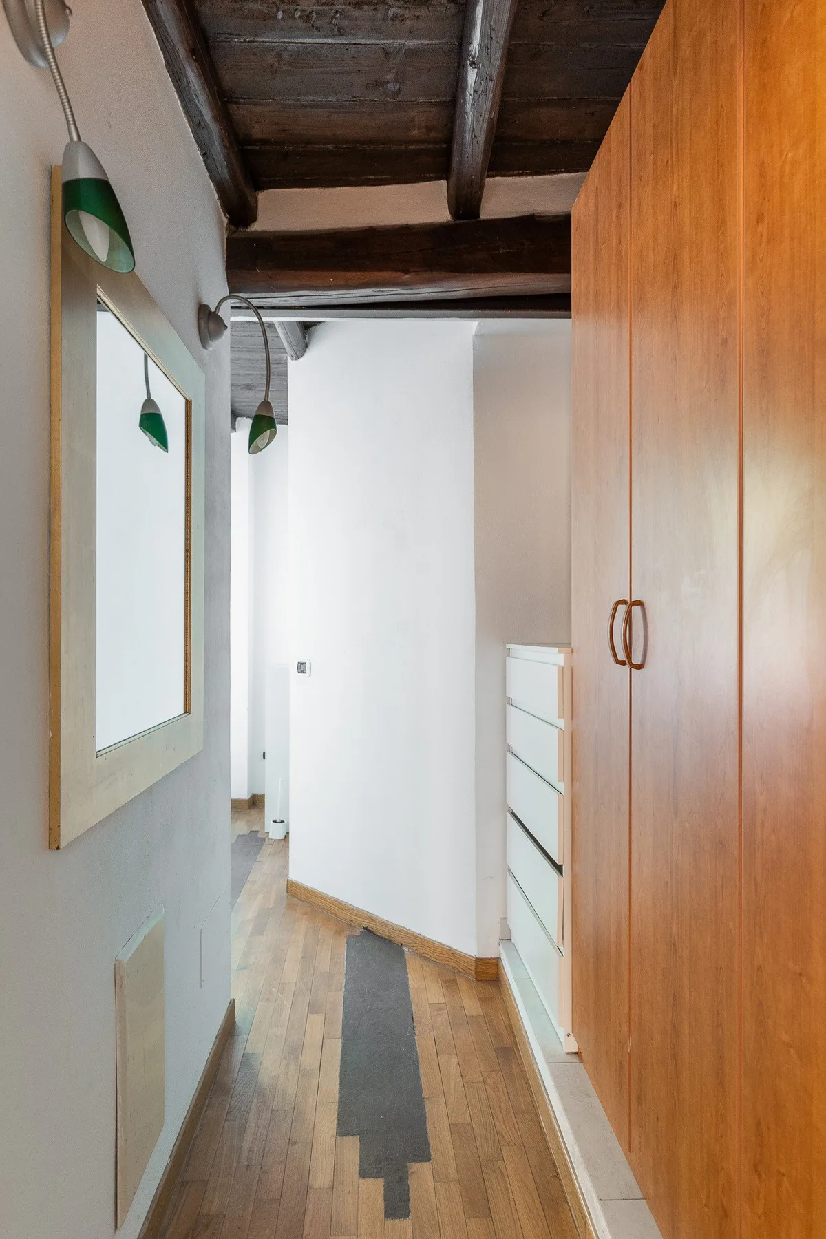 A narrow hallway with wood flooring, a tall wardrobe, and a mirror.