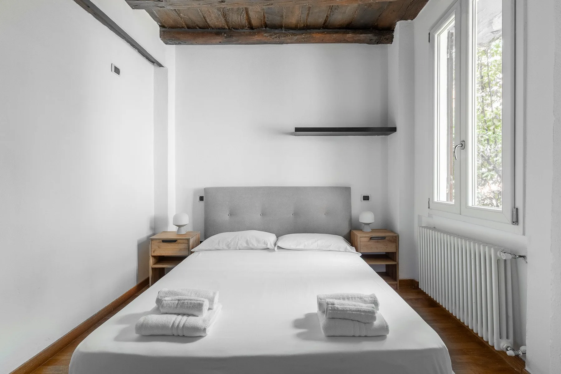 A bright bedroom with a neatly made bed and a large window.