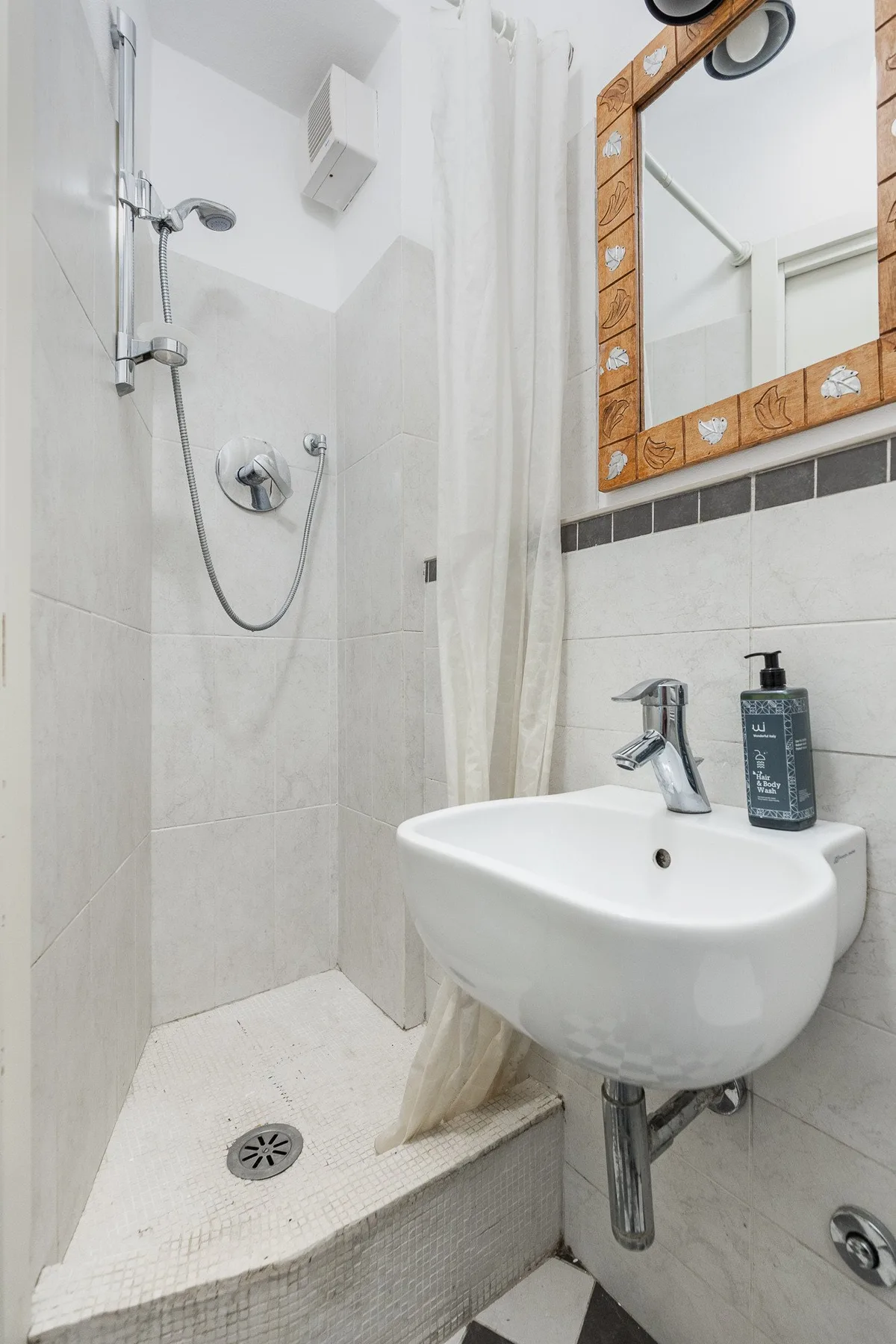 A tiled bathroom with a wall-mounted shower, sink, and mirror.