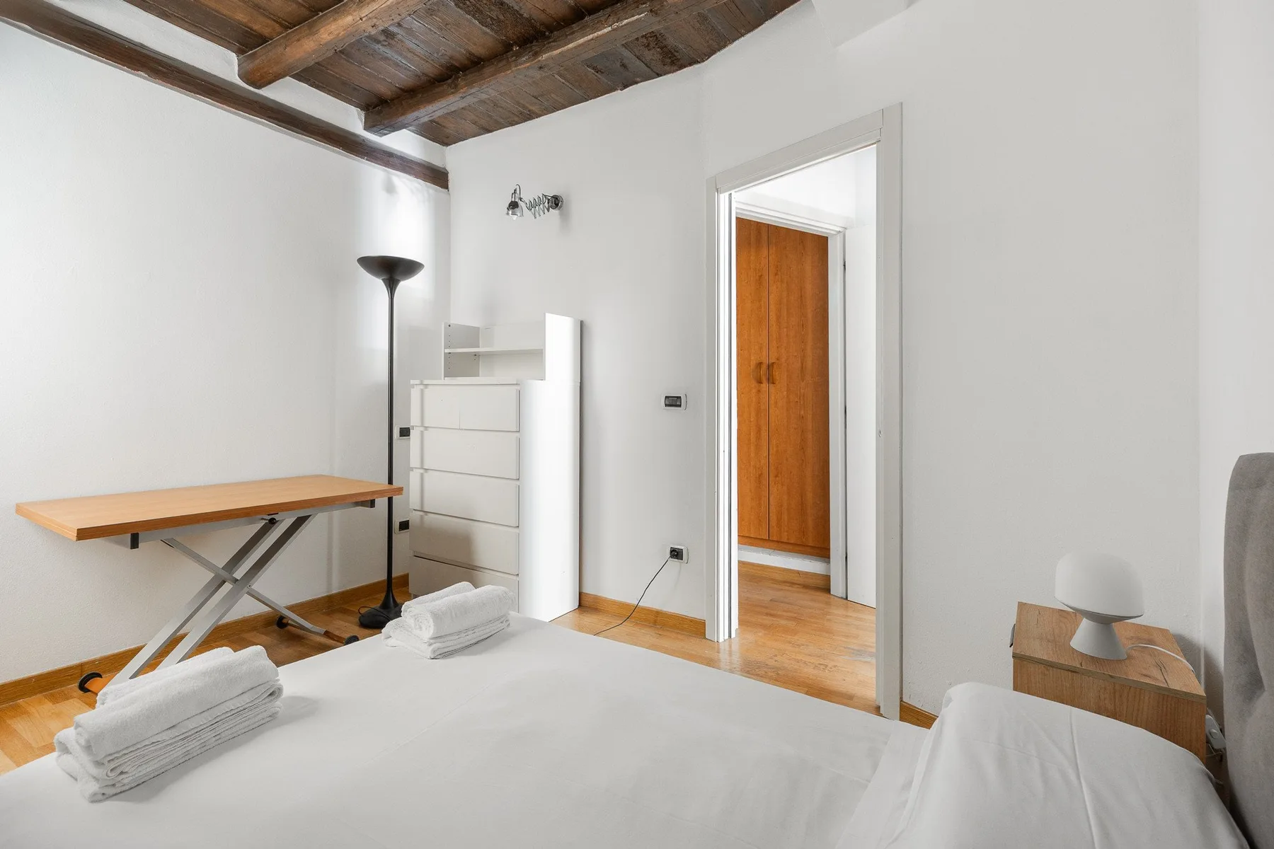 A bright bedroom with a bed, a wooden ceiling, and a doorway to another room.