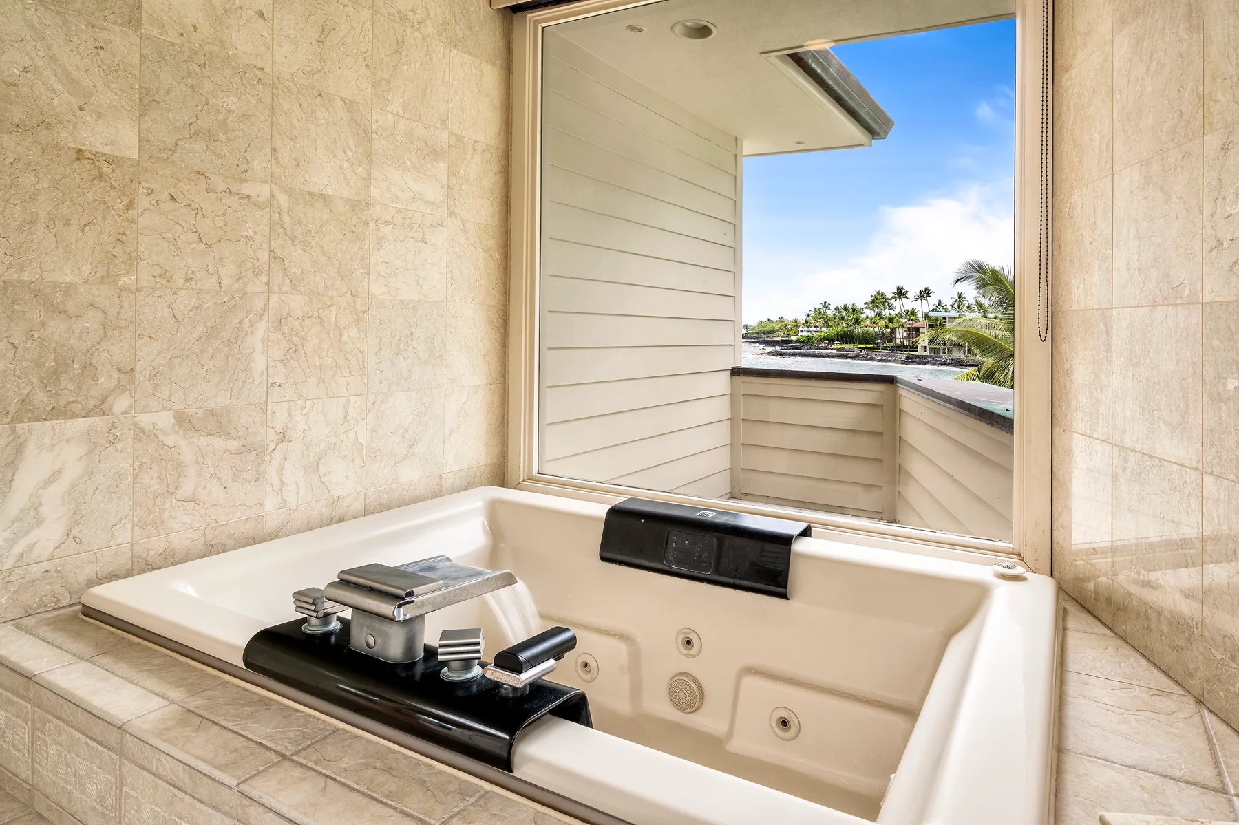 Una bañera empotrada está junto a una ventana abierta con vista a palmeras y agua.