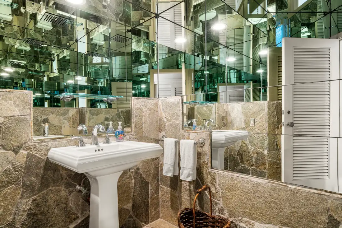 Un baño con un lavabo de pedestal, paredes de azulejos y superficies espejadas.