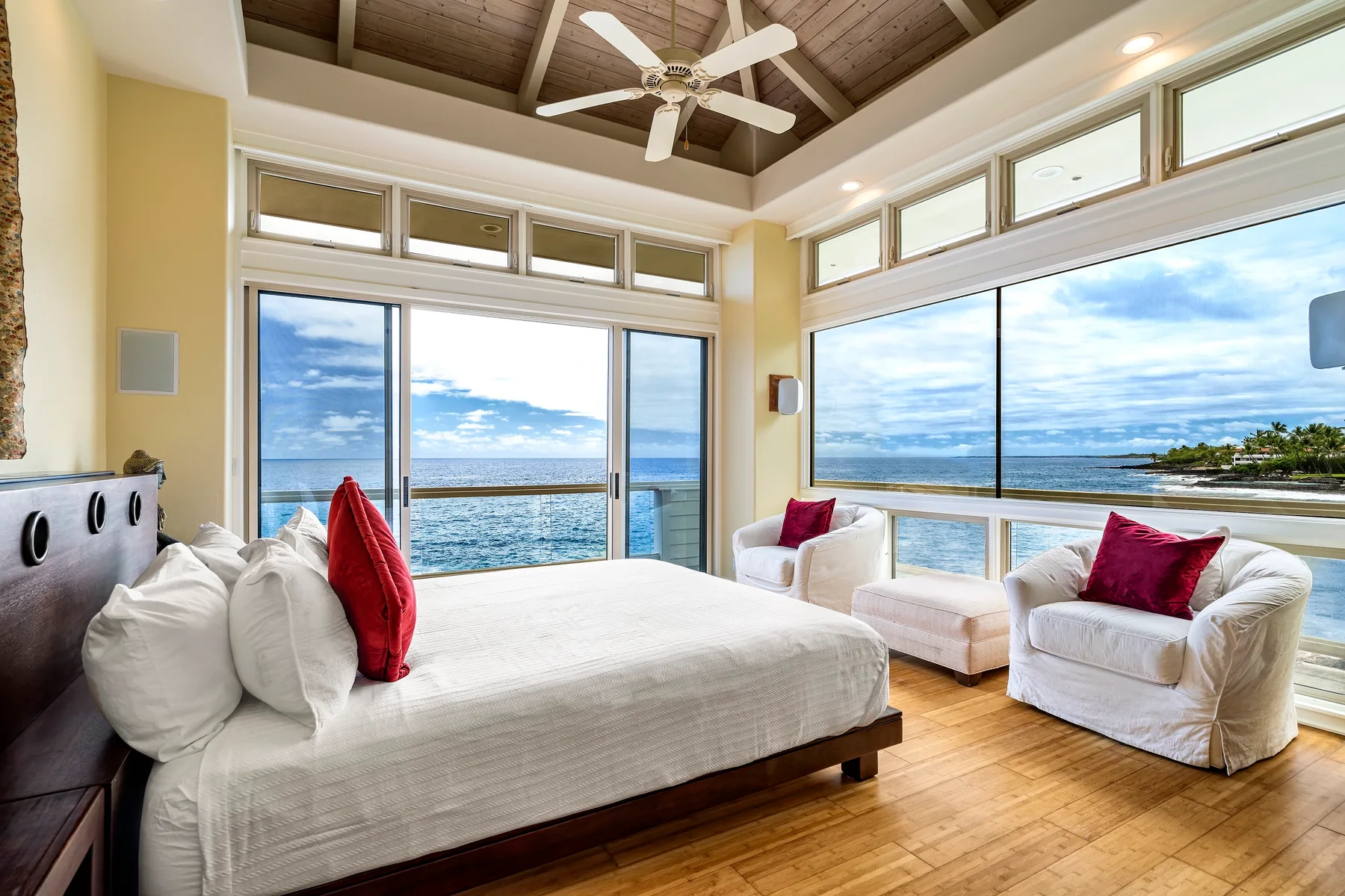 Un dormitorio luminoso con cama y asientos junto a grandes ventanas con vistas al océano.
