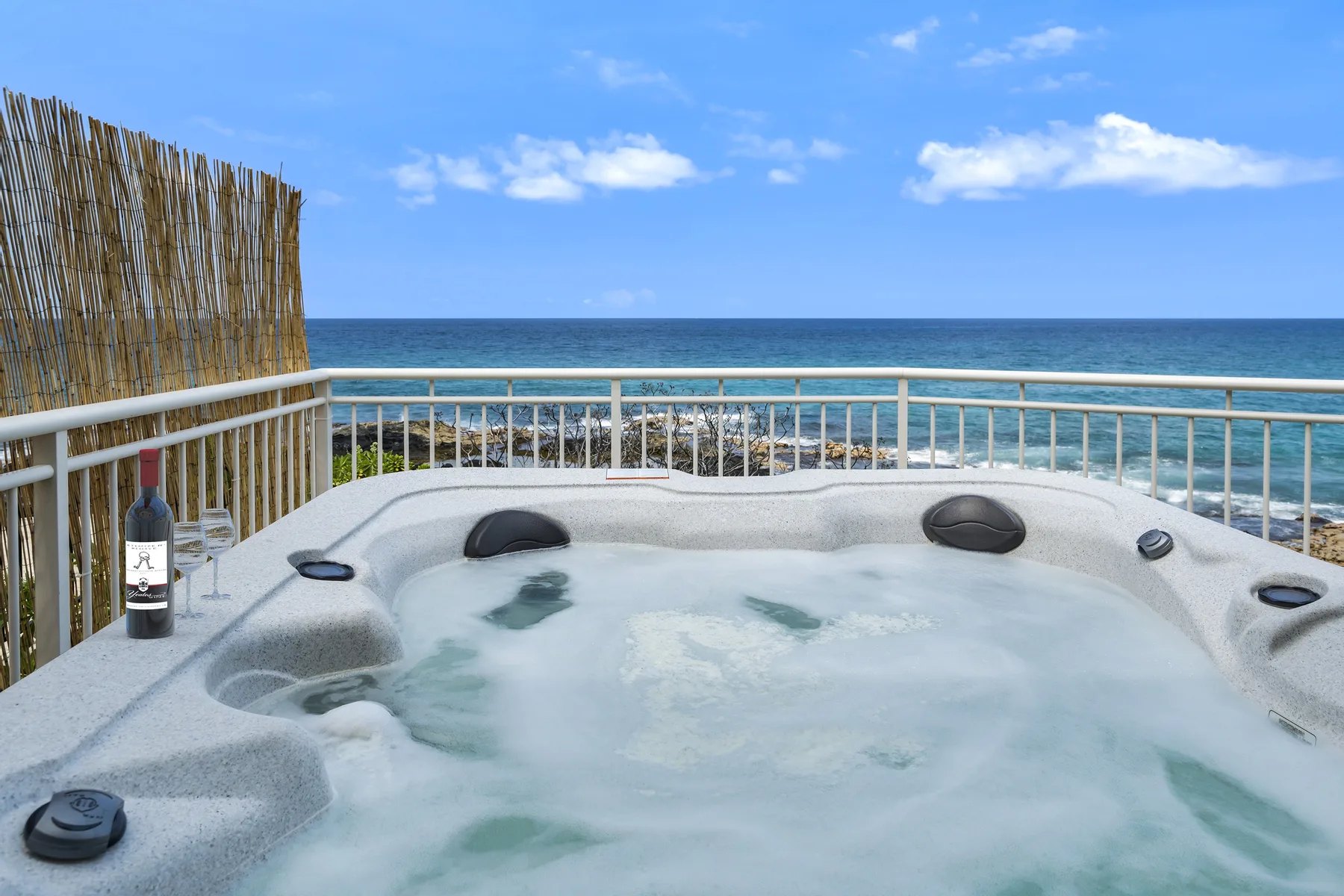 Un jacuzzi al aire libre da al océano, con una barandilla blanca junto a la terraza.