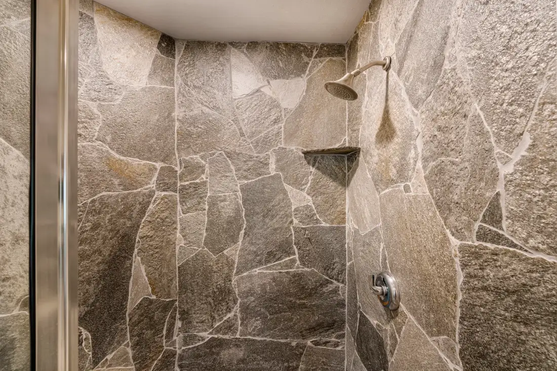 Una zona de ducha con azulejos, cabezal y controles montados en la pared.