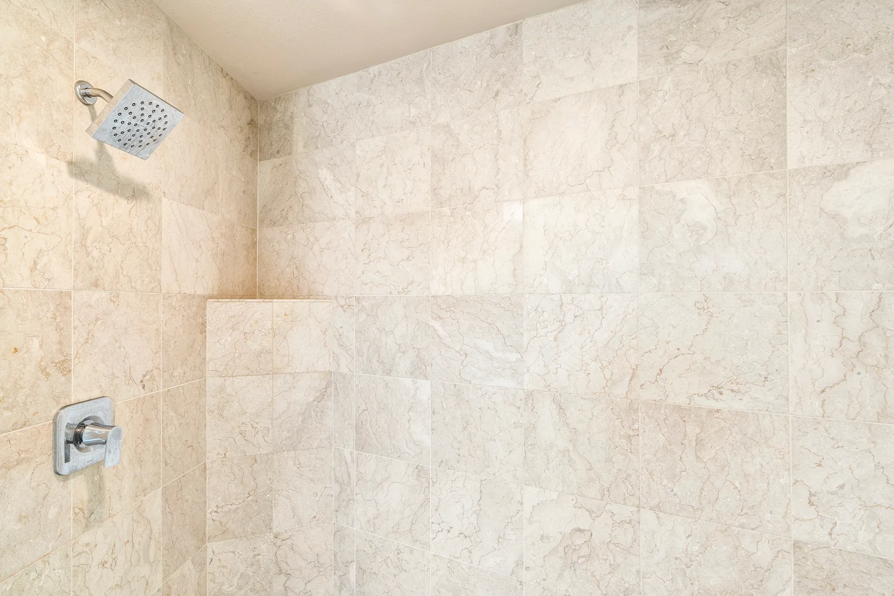 Una zona de ducha con azulejos, ducha de pared y control.