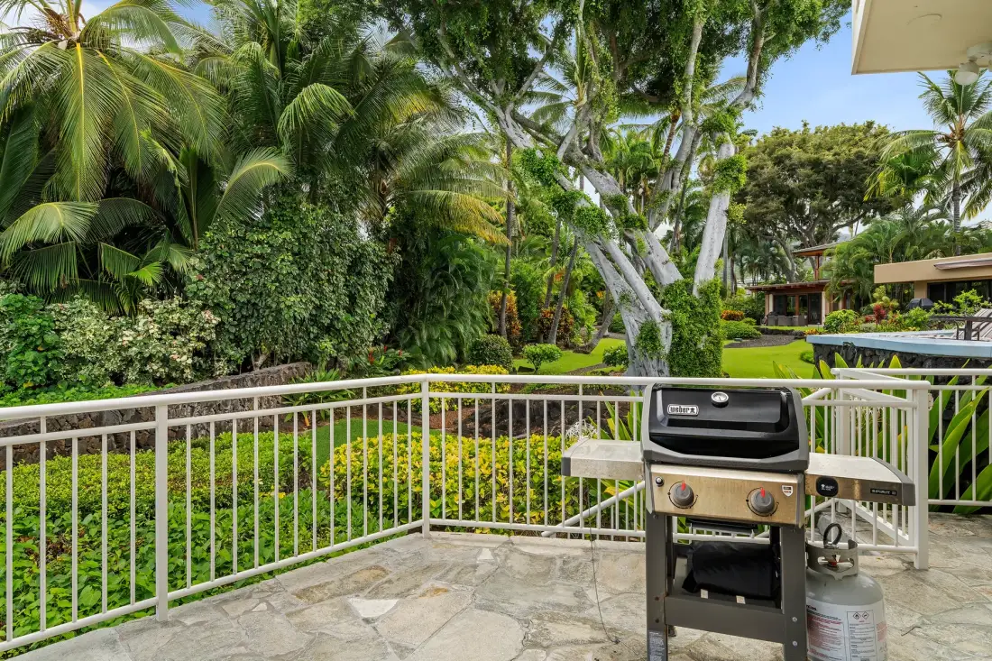 Un patio de piedra con una parrilla da a un exuberante jardín tropical.