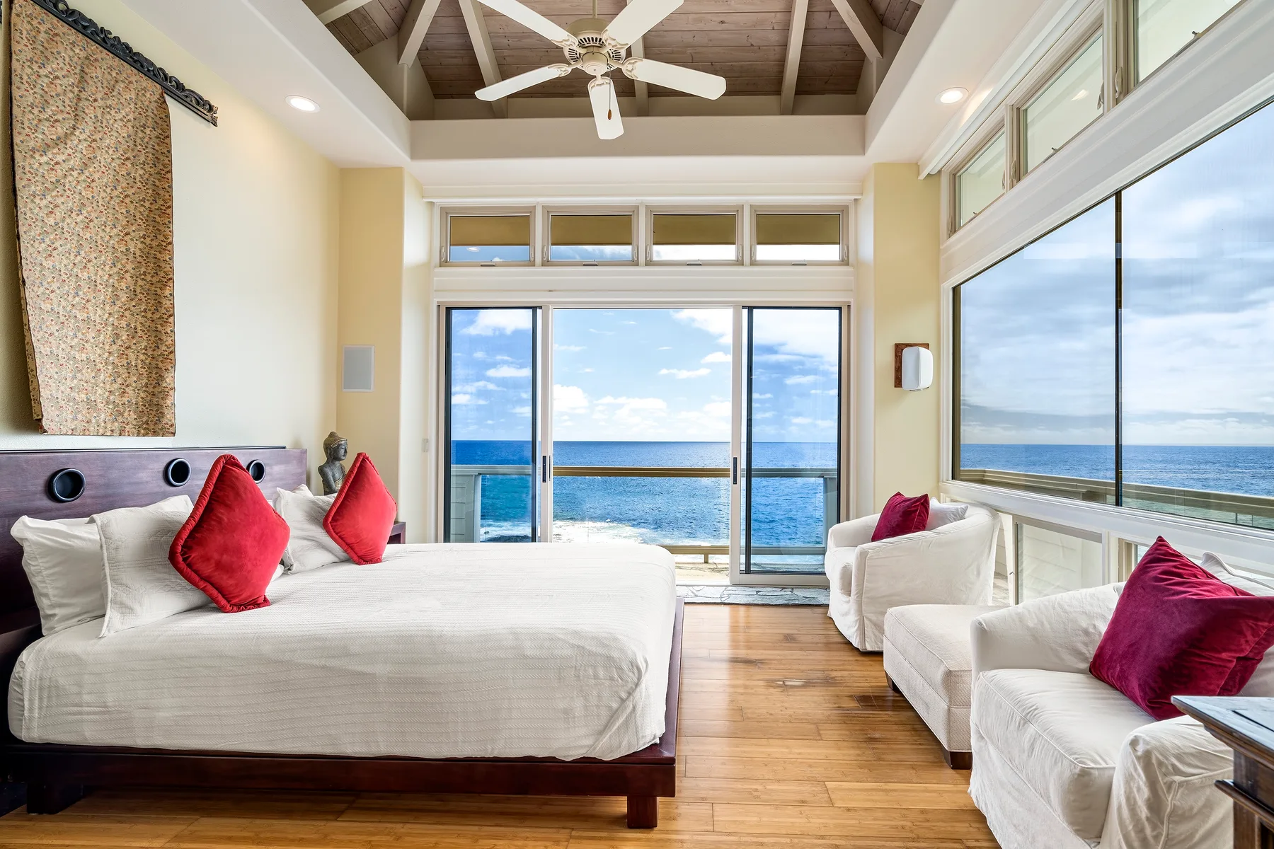Un dormitorio con una cama grande, asientos y amplios ventanales con vista al océano.