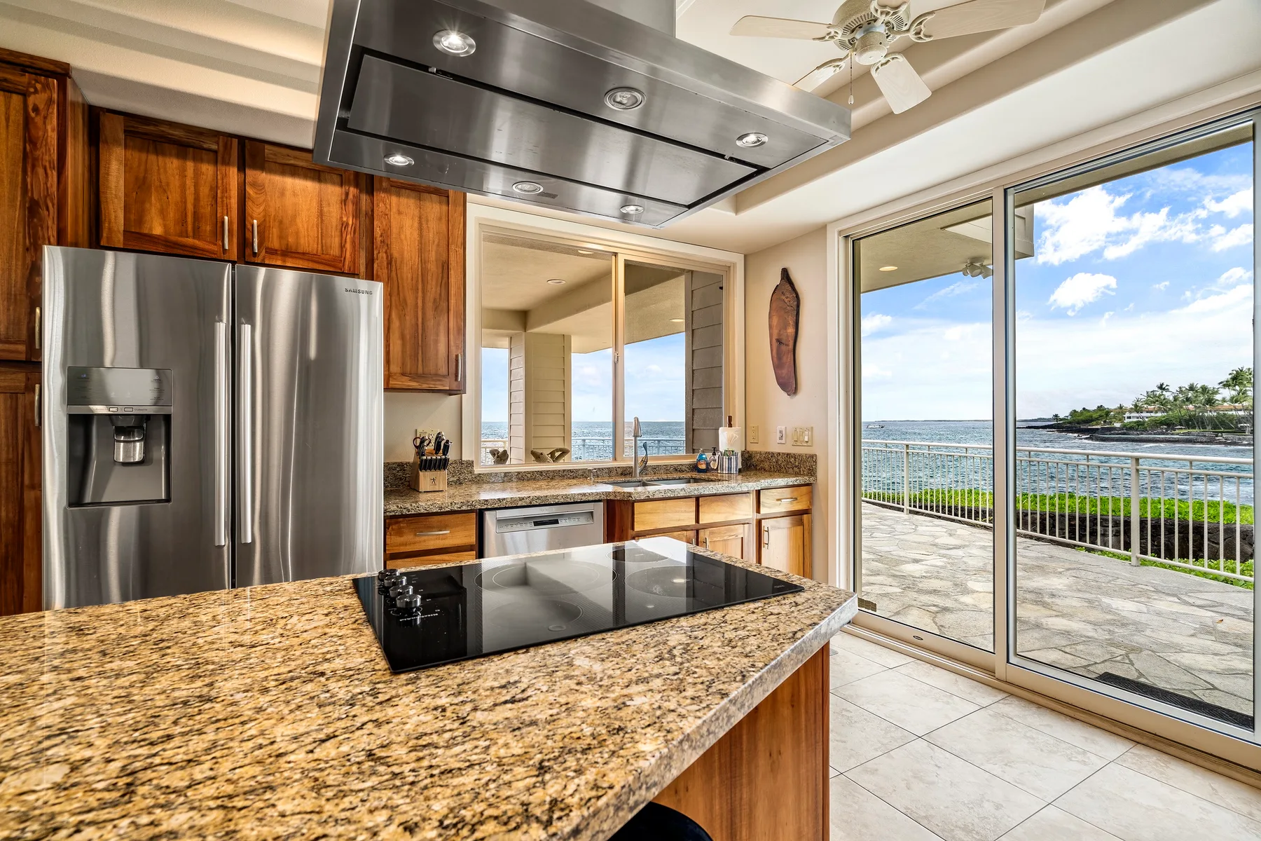 Una cocina luminosa con una isla de granito y puertas corredizas de vidrio con vista al agua.