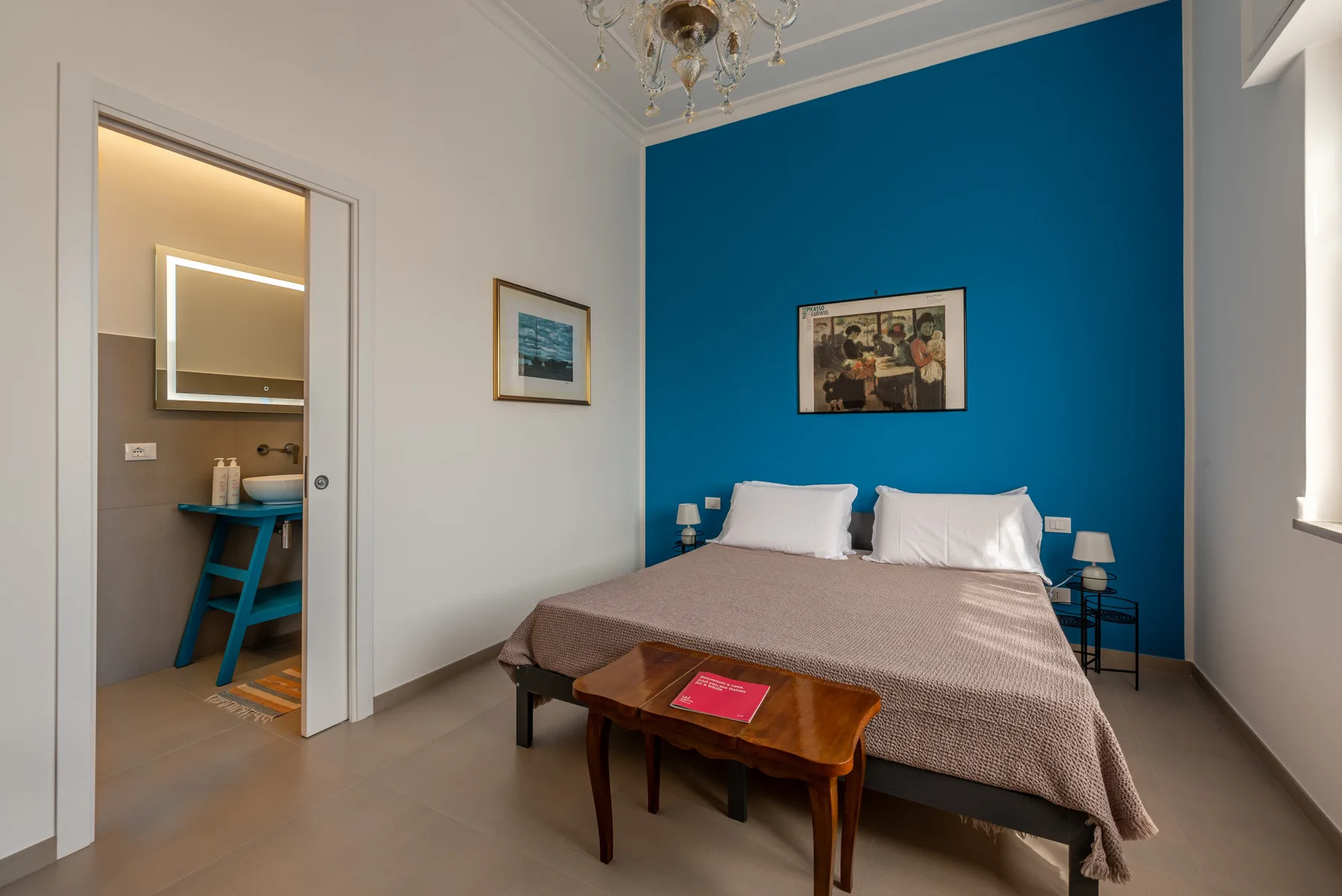 A bedroom with a double bed against a blue accent wall and a wooden table.