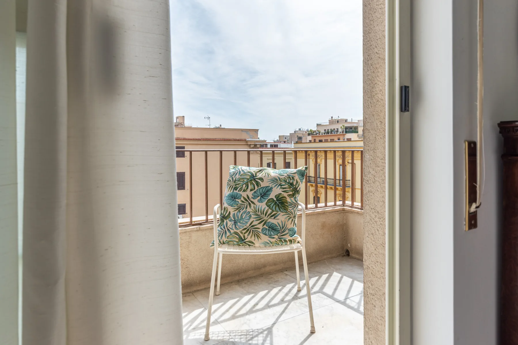 A balcony with a patterned chair overlooks nearby buildings.